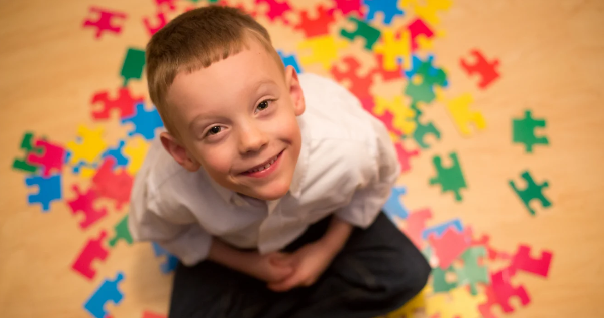 boy looking at the camera with puzzle pieces at the floor